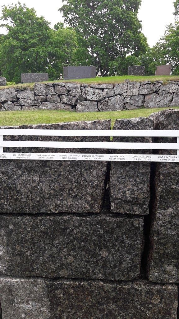 Kivimuuri, jossa on valkoisia vaakasuoria raitoja, jonka takana on nurmialue ja puita.