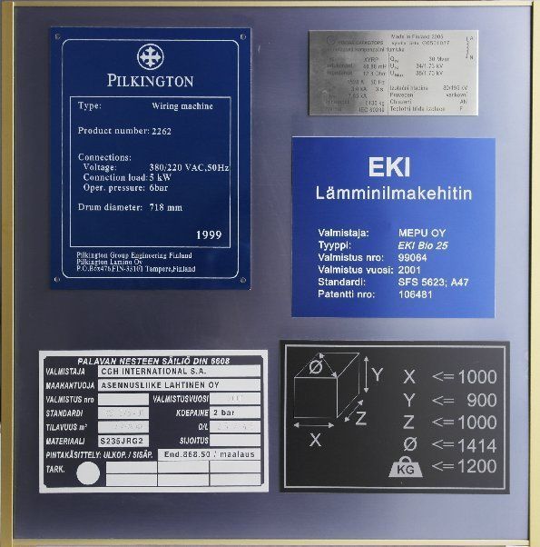 Sinisiä teollisuusnimikylttejä ja vaatimustenmukaisuustarroja kiinnitettynä seinäpaneeliin.