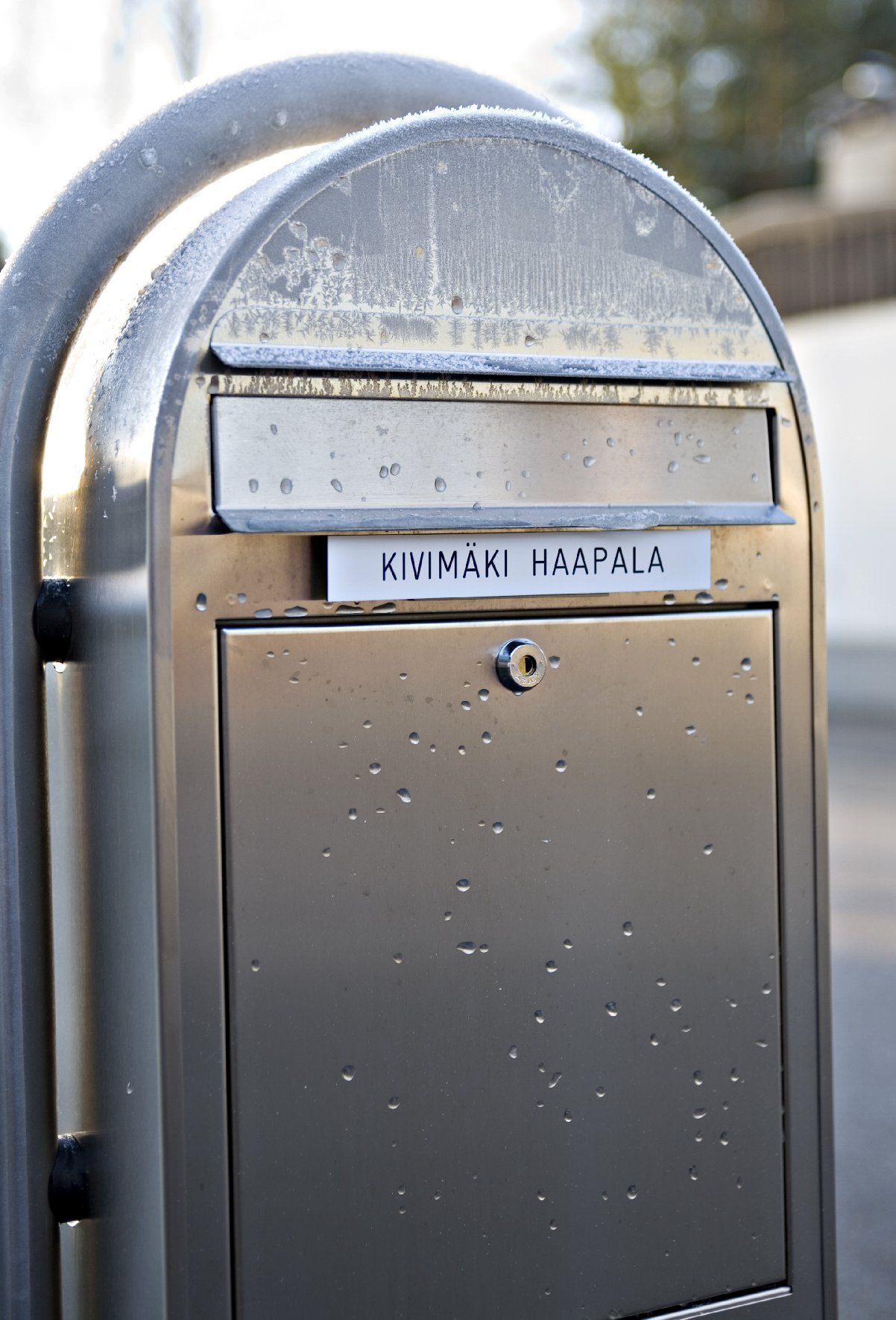 Metallinen julkinen postilaatikko, jossa on postiluukku ja nimikyltti pylväässä ulkona
