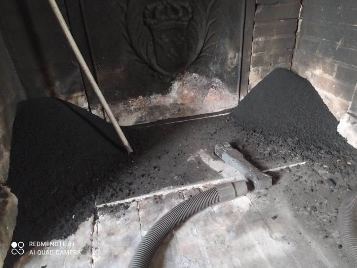 Une personne nettoie une cheminée ; on aperçoit un gros tas de suie et un tuyau d’aspirateur.