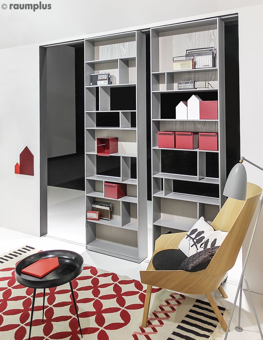 Ein Wohnzimmer mit einem Stuhl, einem Tisch und Regalen mit dem Wort raumplus auf der Unterseite