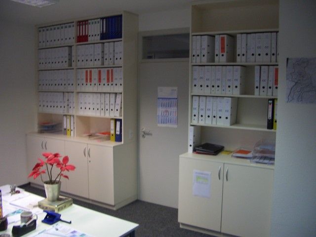 Ein Zimmer mit einem Schreibtisch und Regalen voller Ordner