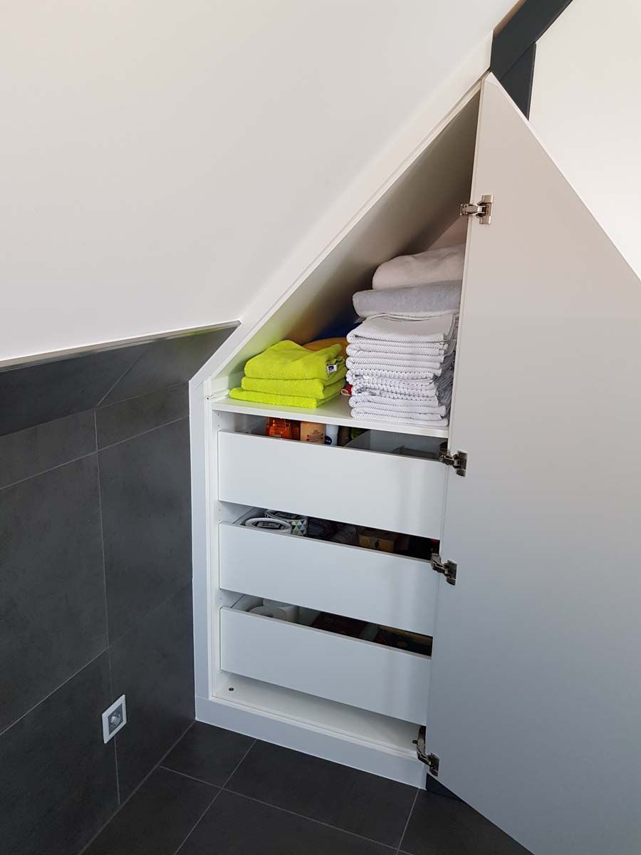 Ein weißer Schrank mit Schubladen unter einer Treppe, voller Handtücher.
