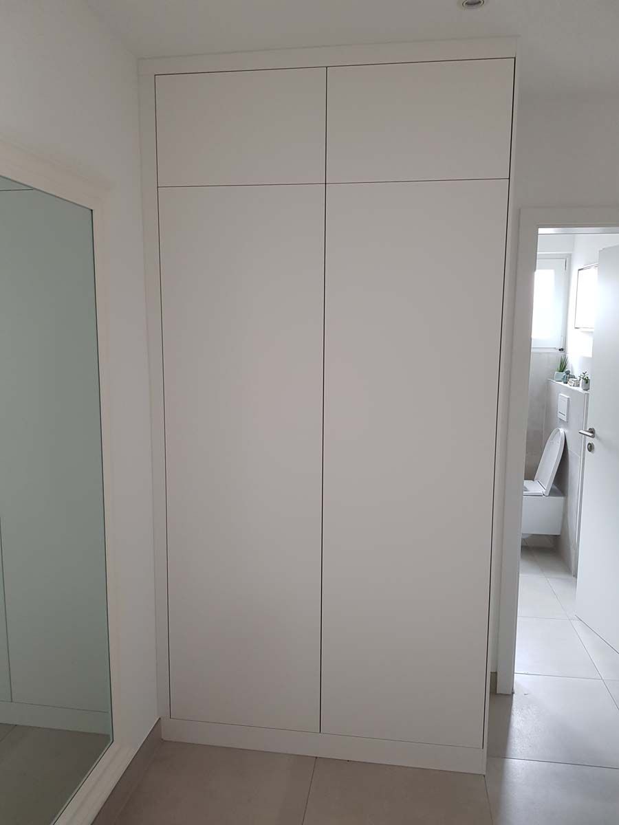 Ein weißer Kleiderschrank in einem Badezimmer neben einer Toilette und einem Spiegel.