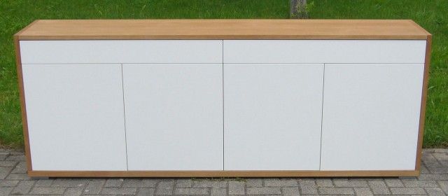 Auf einem Gehweg steht ein Holzschrank mit weißen Türen und Schubladen.