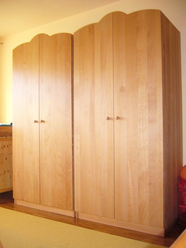 In einem Schlafzimmer steht ein großer Holzkleiderschrank neben einem Bett.