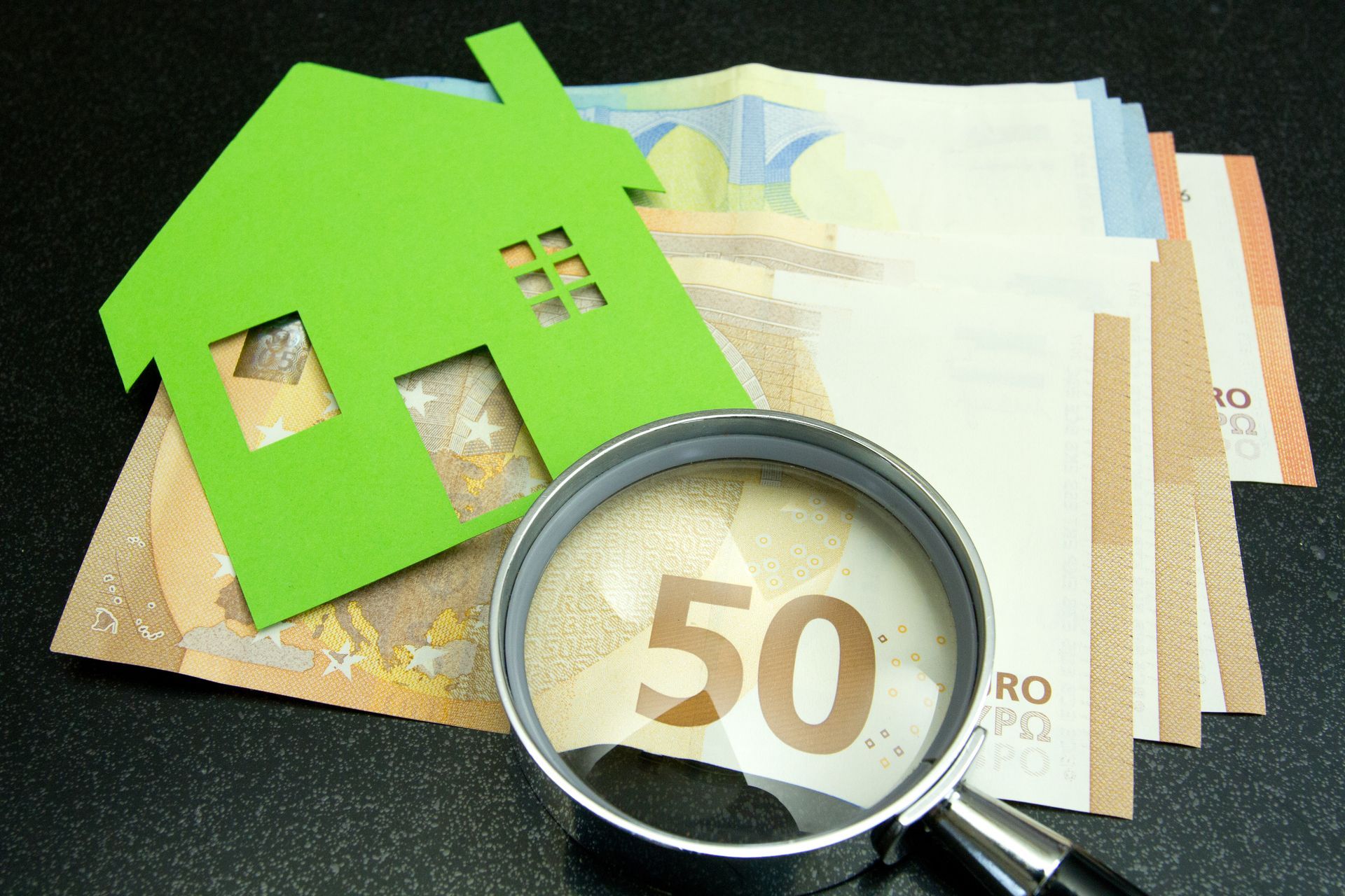 Billets de banque éparpillés sur une table, maquette de maison et loupe posées sur les billets