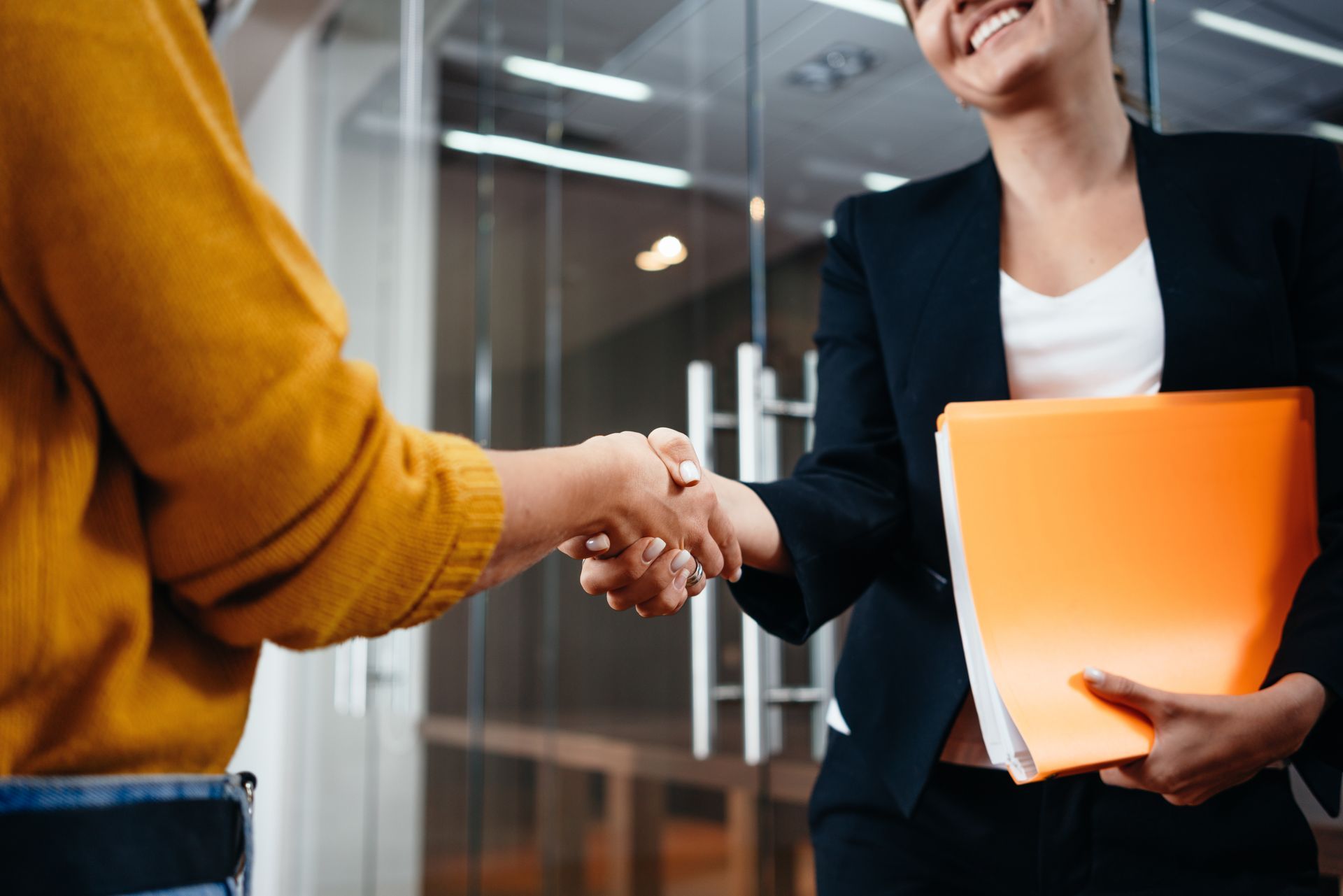 Poignée de main entre deux personnes, l'une d'elles tient des dossiers dans sa main gauche