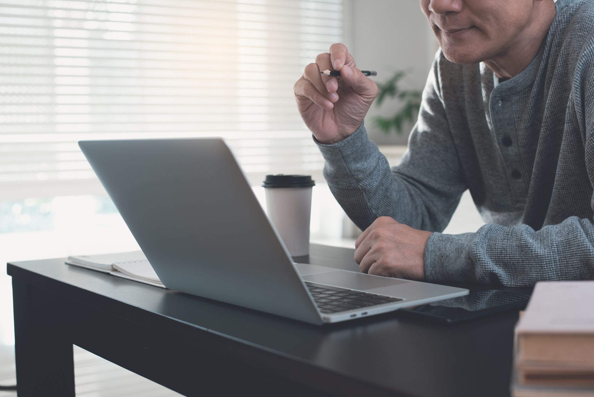 Personne devant son ordinateur, gobelet de café posé sur la table