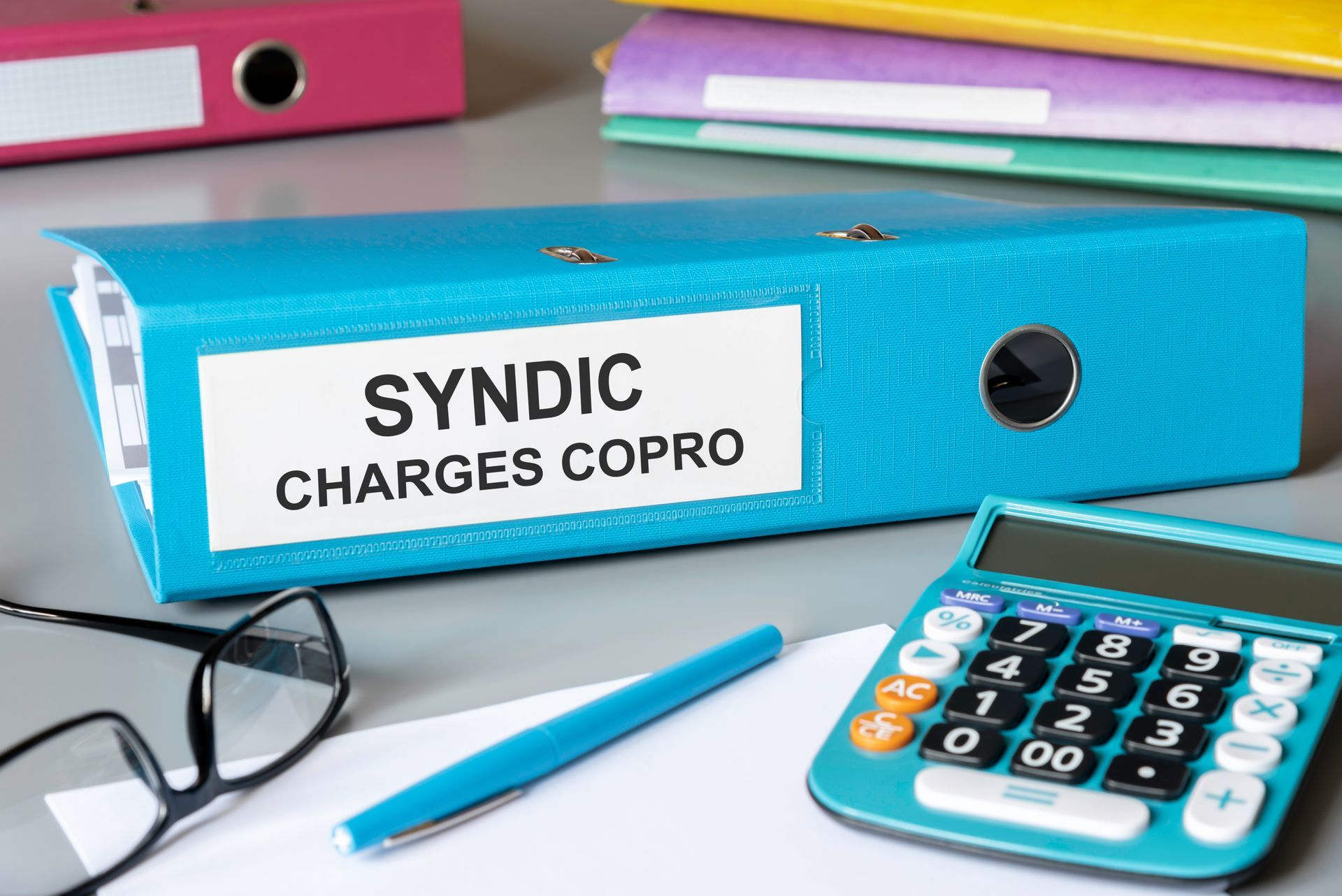 Classeur de charges de copropriété, lunettes, stylo et calculatrice sur une table