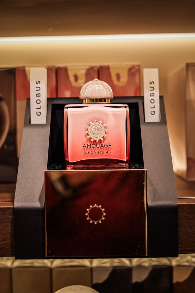 Rosa Parfümflakon mit floralem Muster, umgeben von rosa Blüten und Verpackung auf einer Marmoroberfläche.