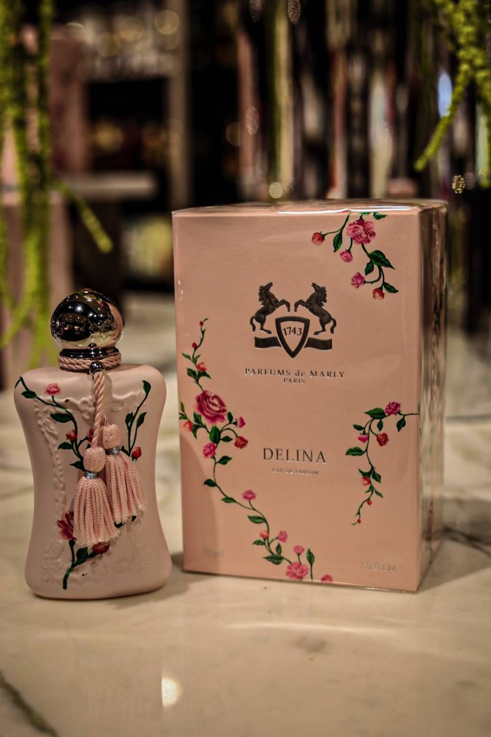 Rosa Parfümflakon und Schachtel mit floralen Akzenten auf Marmoroberfläche.