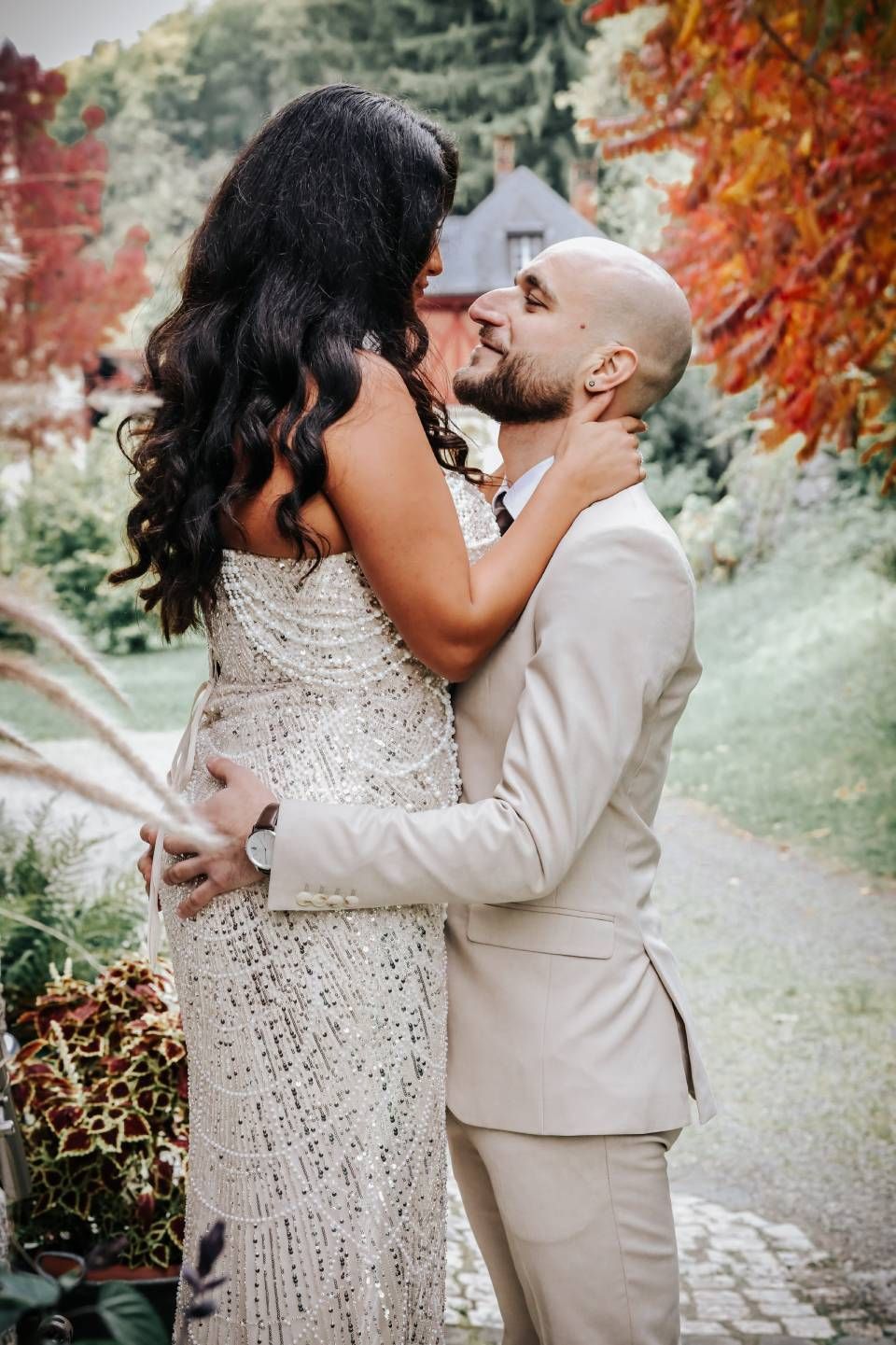 Ein Paar umarmt sich; Frau in einem verzierten Kleid, Mann im Anzug, herbstliche Szenerie im Freien.