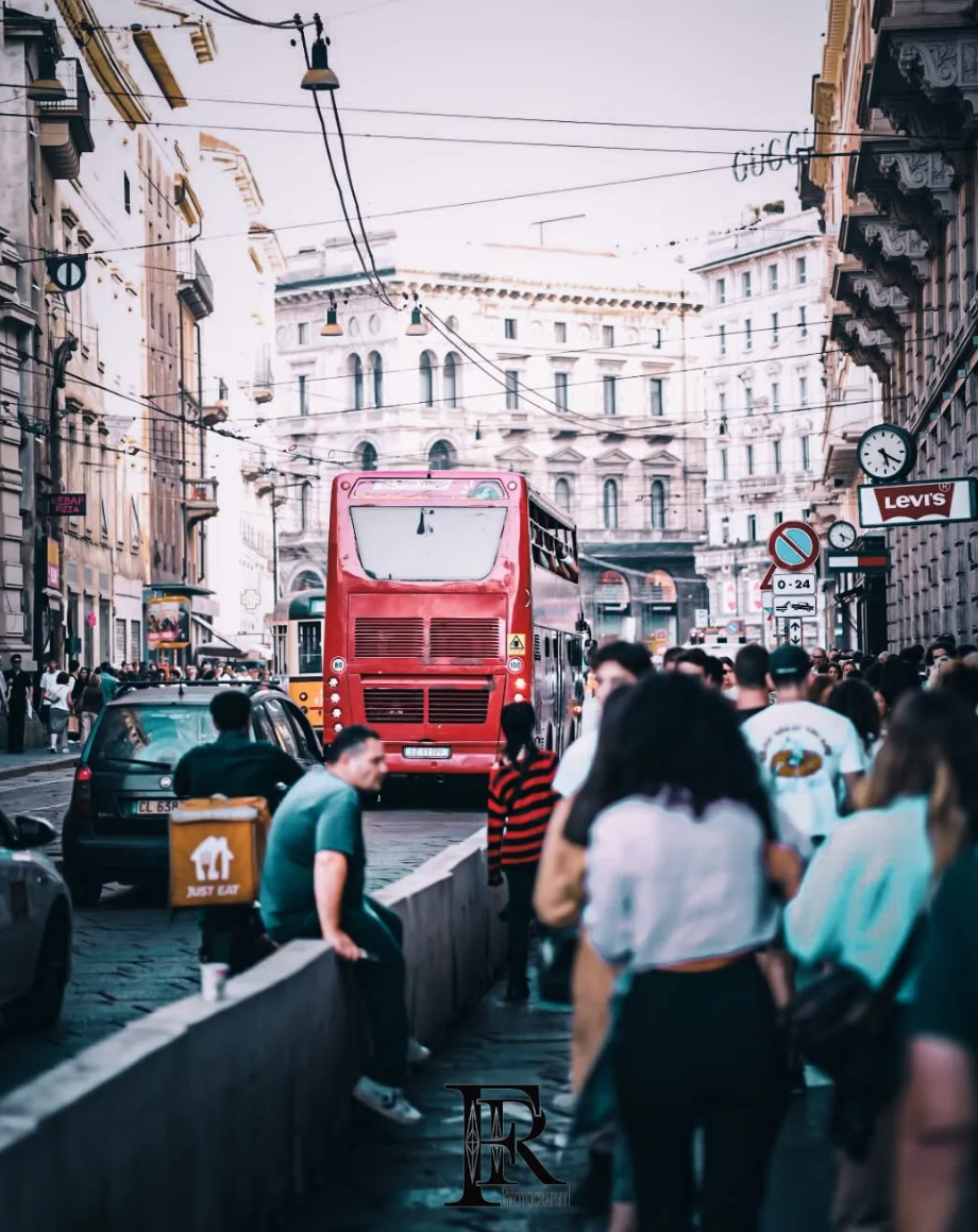 Ein Mann in weisser Kleidung sitzt auf einer Bank und blickt nach unten. Schwarze Stiefel. Draussen.