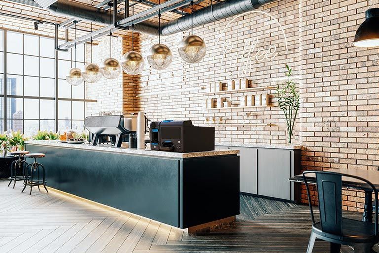 Área de recepción de oficina moderna con escritorio negro, paredes de ladrillo, lámparas colgantes y suelo de madera.