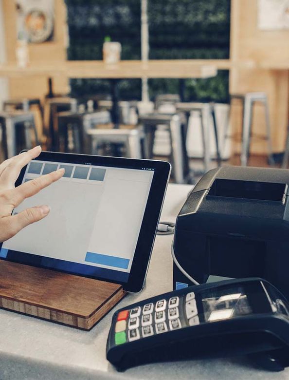 Tableta, lector de tarjetas y terminal de pago en la barra de una cafetería con asientos borrosos al fondo.