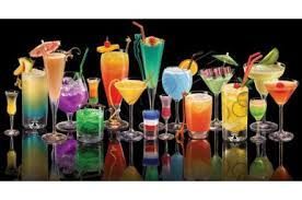 Un assortiment de cocktails colorés dans des verres de formes et de tailles variées, disposés sur un fond noir réfléchissant.