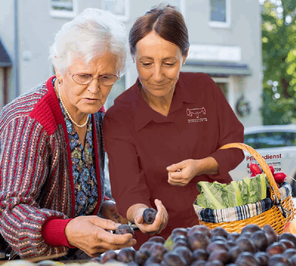 Pflegerin begleitet und unterstützt eine Seniorin beim Einkaufen