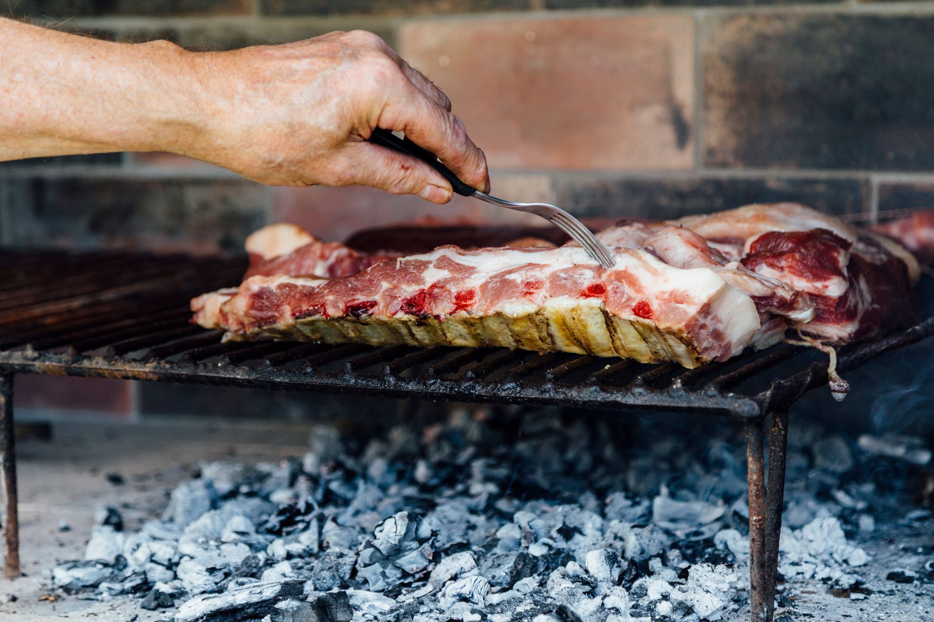 Mano usando un tenedor en costillas asándose sobre carbón.