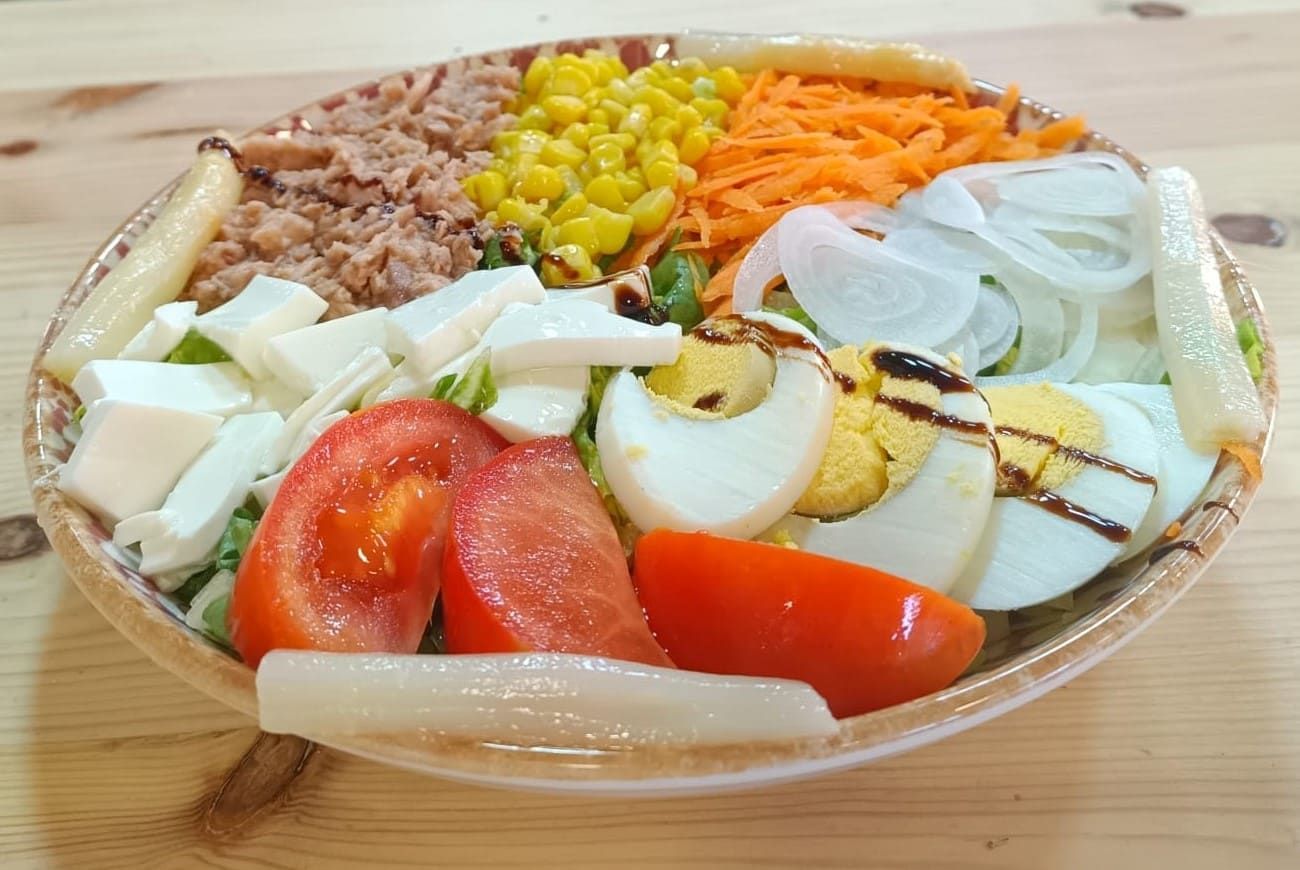Ensaladera: atún, maíz, zanahorias, cebollas, espárragos, queso, tomates, huevos, sobre una mesa de madera.