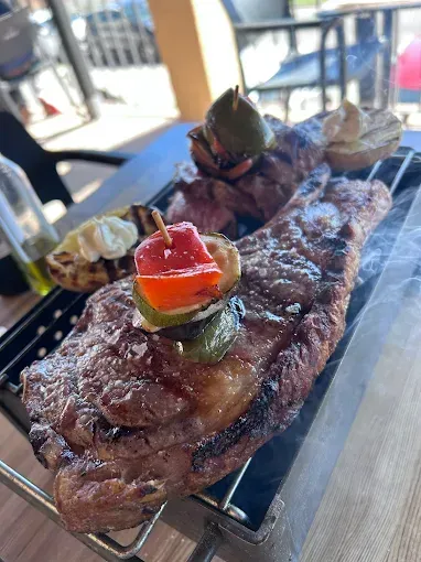 Filete a la parrilla con verduras y salsa sobre una rejilla metálica, en un entorno al aire libre.
