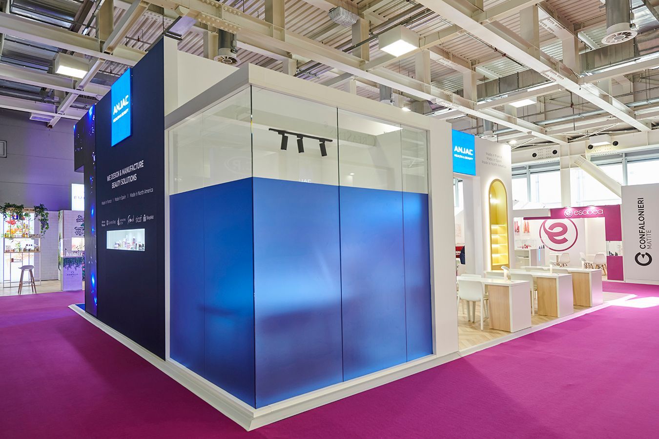 Un stand d'exposition présentant une grande structure d'angle en verre translucide bleu et un intérieur lumineux et ouvert sur une moquette violette.
