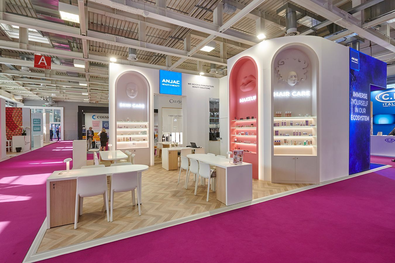 Un stand d'exposition moderne avec des présentoirs arqués et lumineux pour les cosmétiques, des tables blanches et des chaises sur un tapis rose.