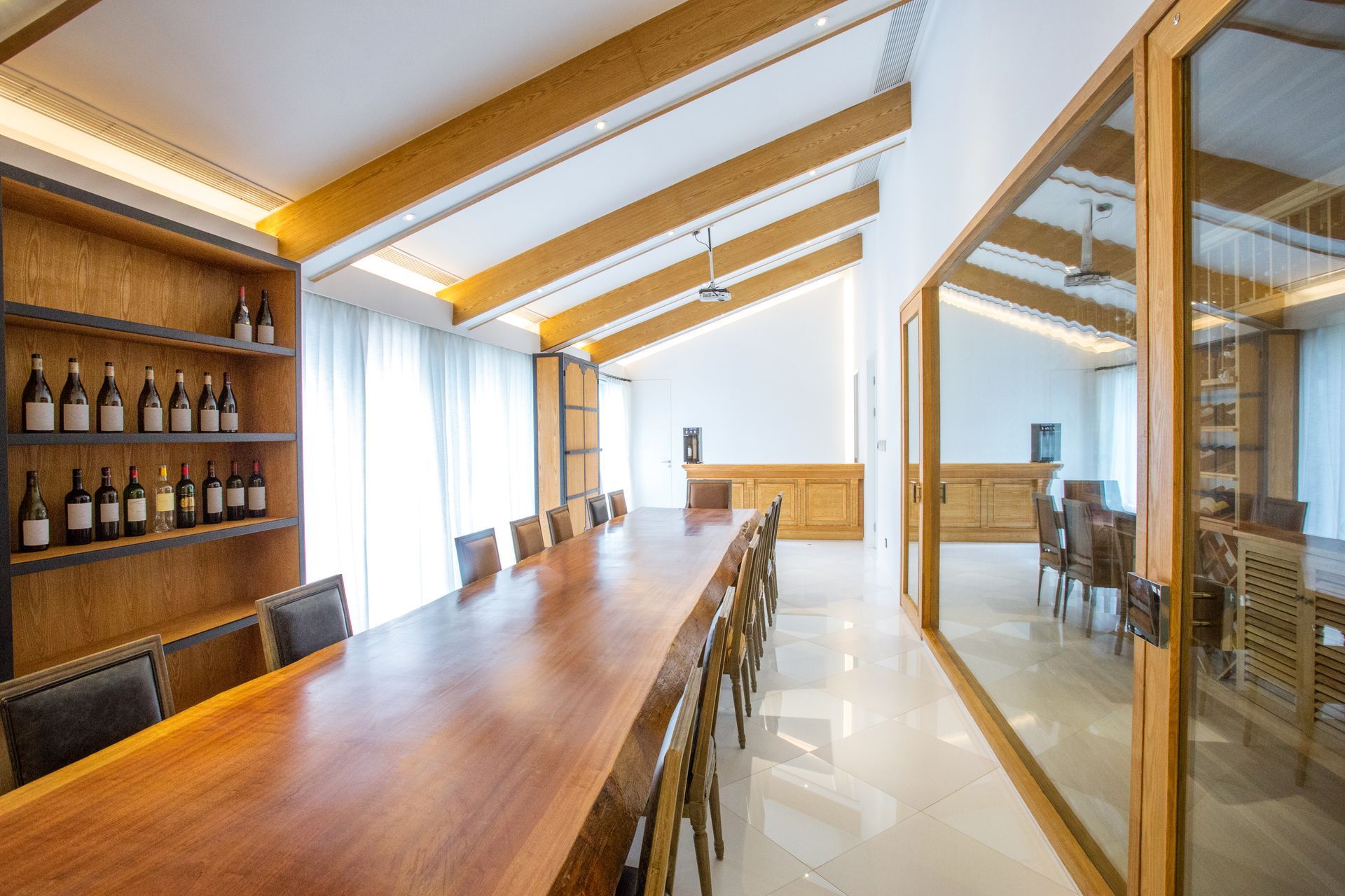 Grande salle de réunion avec immense table en bois et étagères où sont déposées des bouteilles de vin