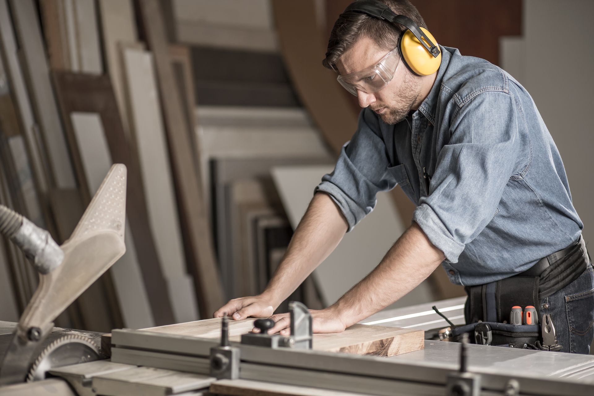 Homme dans un atelier qui découpe un panneau en bois avec des lunettes de protection et un casque antibruit