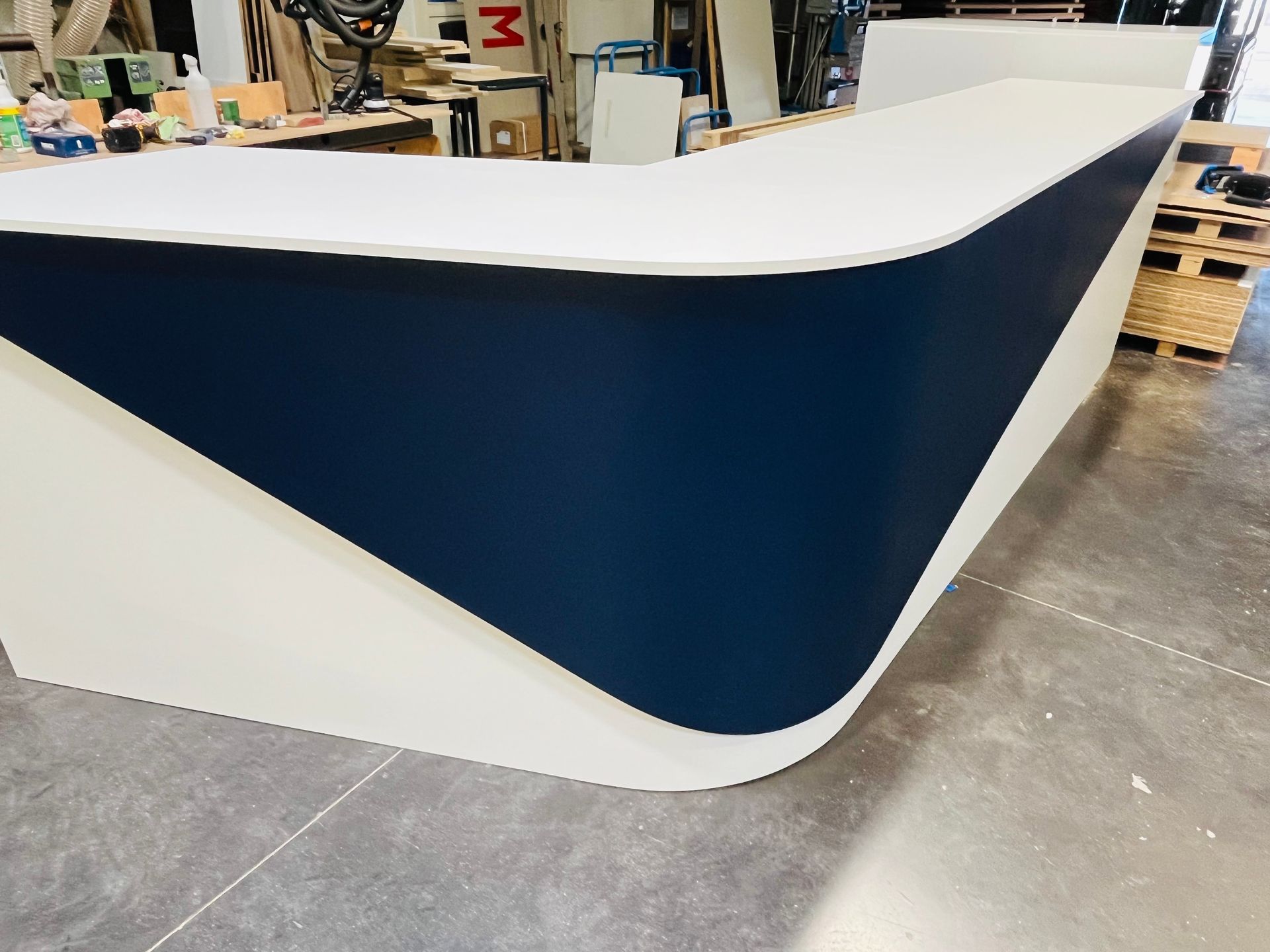 Bureau d'accueil incurvé blanc et bleu marine dans un atelier.