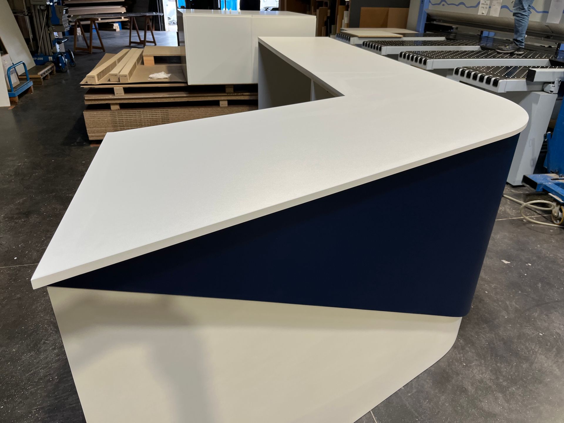 Bureau d'accueil blanc et bleu marine à façade inclinée, dans un atelier.