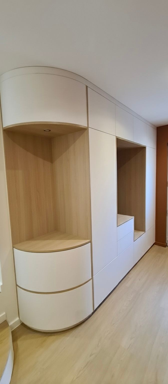 Meubles sur mesure en bois clair et blanc, avec une étagère ouverte incurvée et une niche de rangement centrale encastrée dans une pièce.