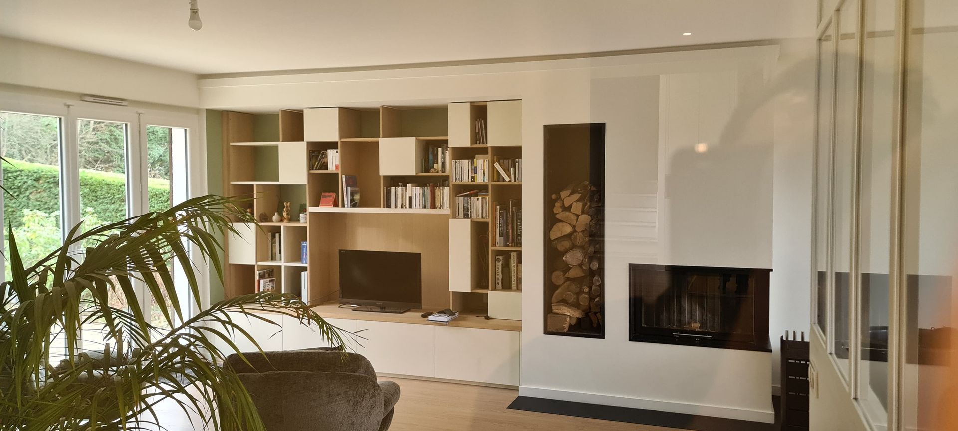 Un salon moderne comprend un meuble mural blanc avec des étagères ouvertes, une télévision et une cheminée attenante.