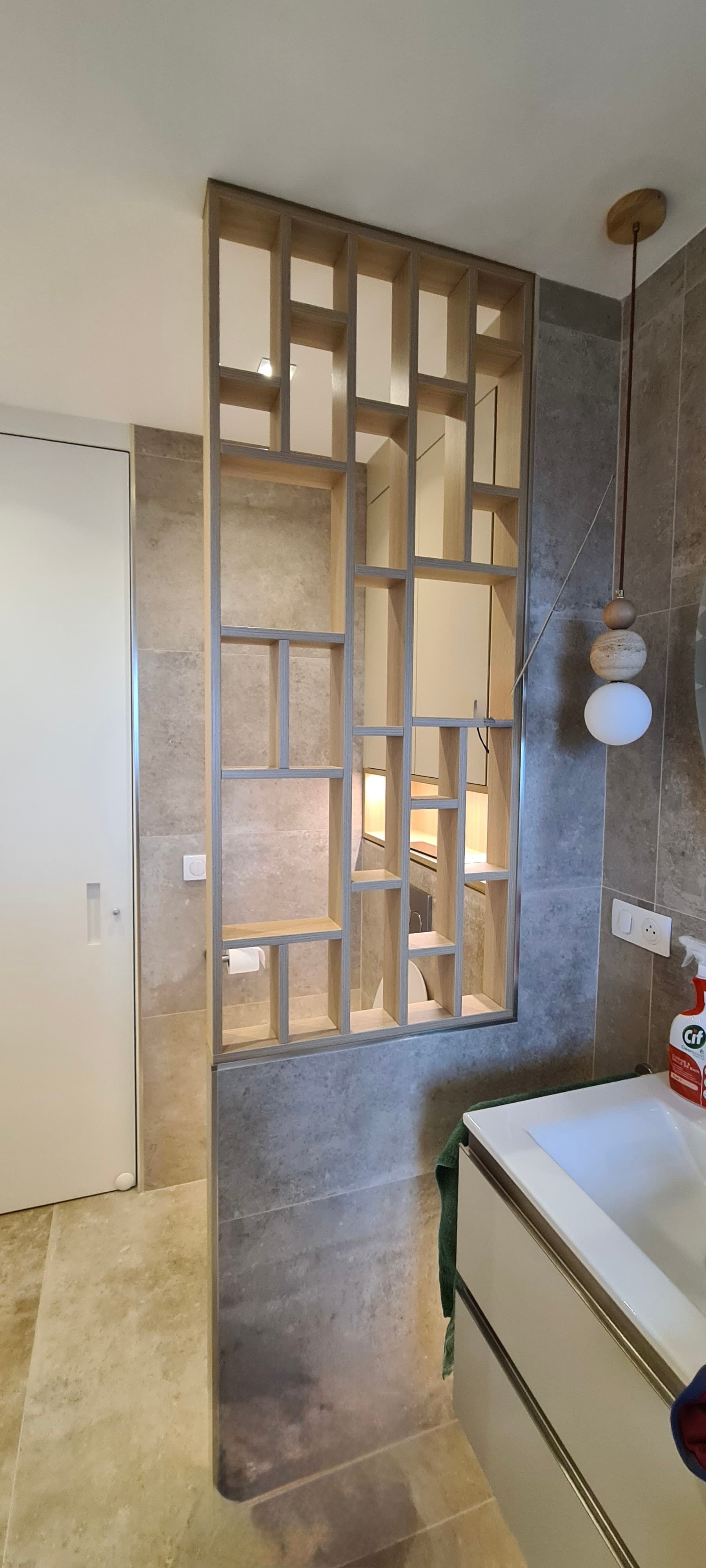 Une cloison verticale en lattes de bois à motif quadrillé asymétrique, installée entre des murs en pierre dans une salle de bains.
