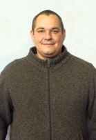 Ein Mann in einem braunen Pullover lächelt in die Kamera.