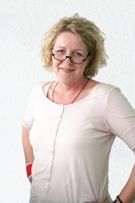 Eine Frau mit Brille und weißem Hemd steht mit den Händen auf den Hüften.