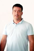 Ein Mann in einem hellblauen Poloshirt steht vor einer weißen Wand.