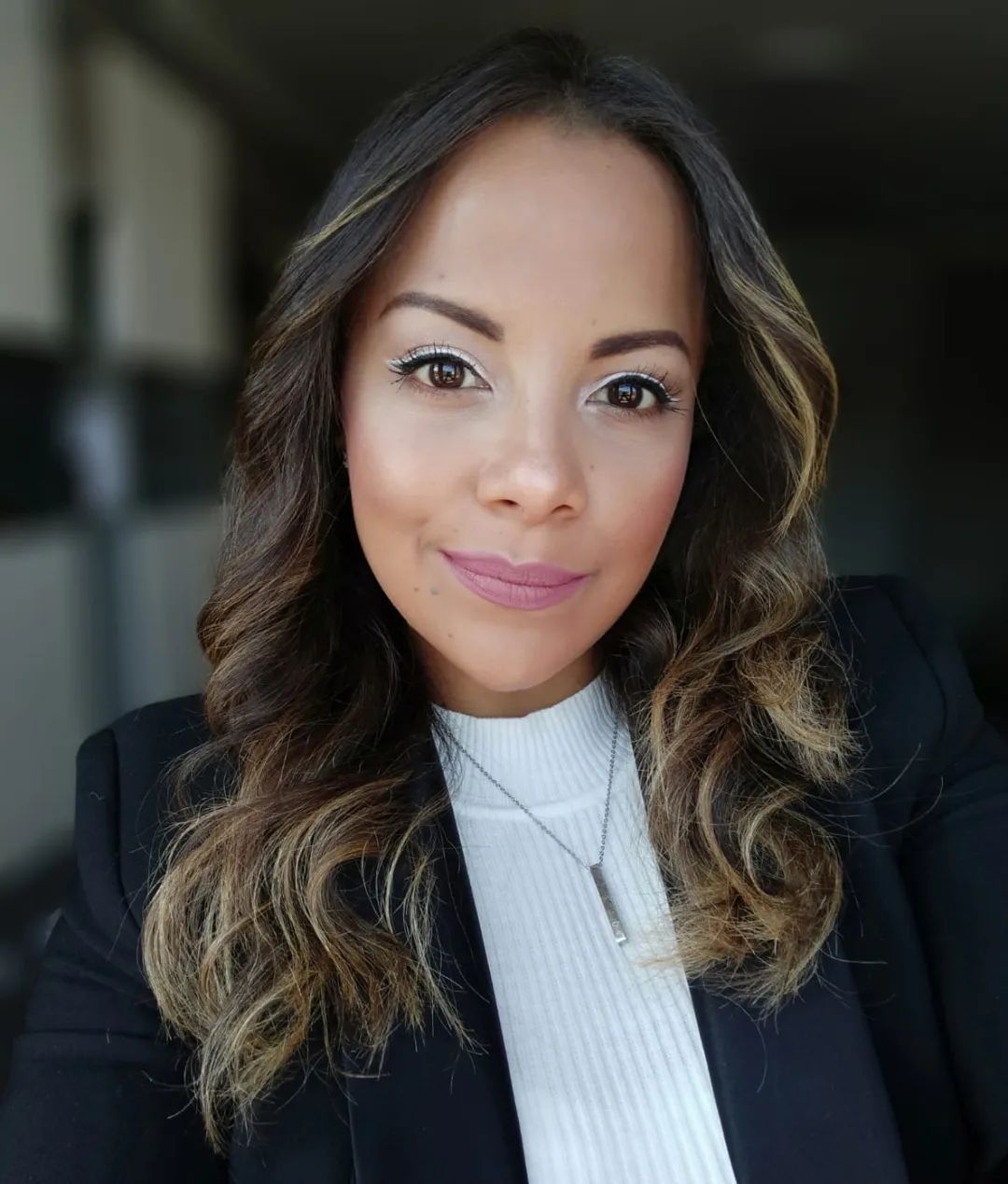 Mujer de cabello castaño, vestida con un blazer negro y un cuello alto blanco, sonriendo.