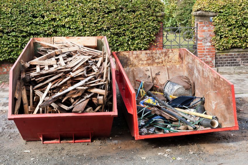 Zwei mit Holz und Müll gefüllte Müllcontainer stehen nebeneinander am Straßenrand.