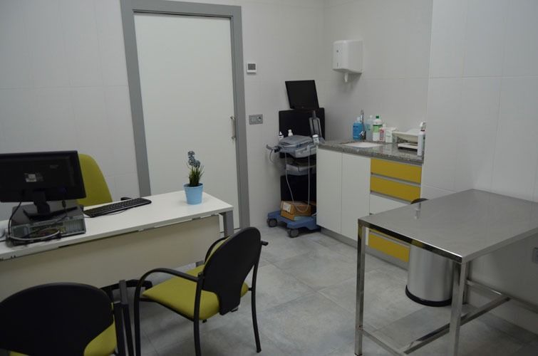 Un consultorio médico con un escritorio y sillas y una mesa de acero inoxidable.