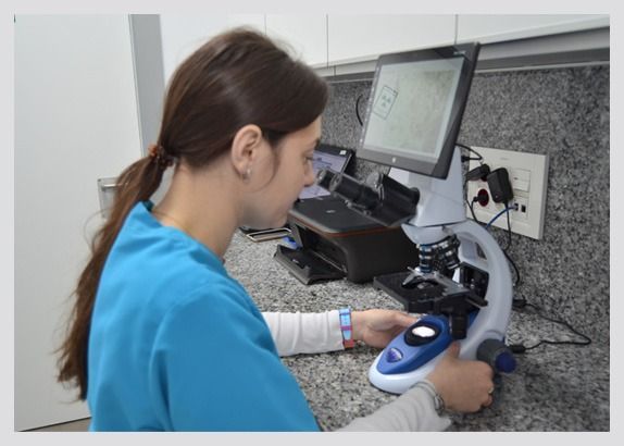 Una mujer con un uniforme azul mira a través de un microscopio.