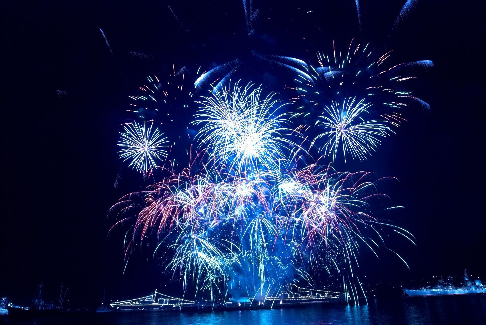 Un montón de fuegos artificiales estallan en el cielo nocturno sobre un cuerpo de agua.
