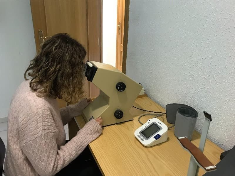 Una mujer está sentada en un escritorio mirando a través de un microscopio.