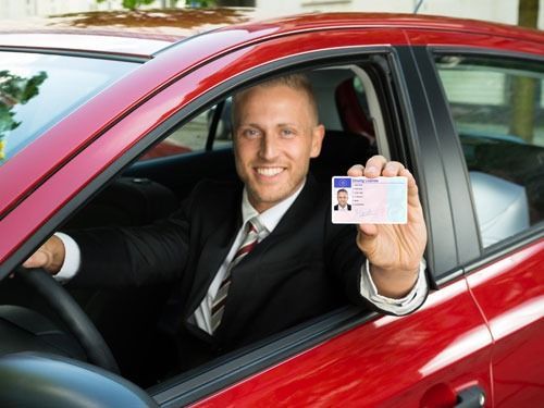 Un hombre está sentado en un coche rojo sosteniendo una licencia de conducir.