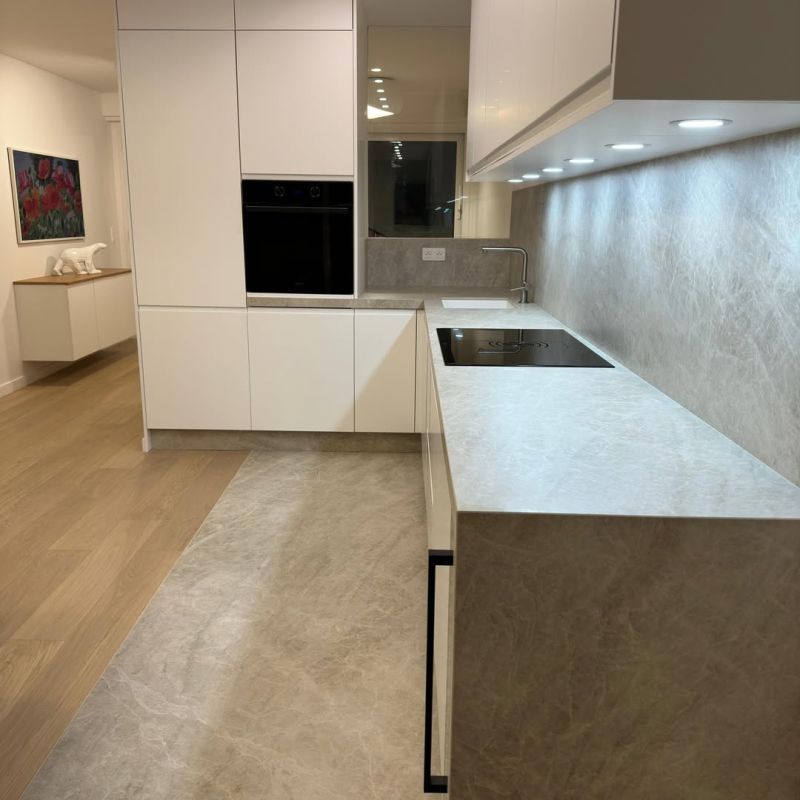 Cuisine moderne blanche et grise avec électroménager intégré et parquet clair.