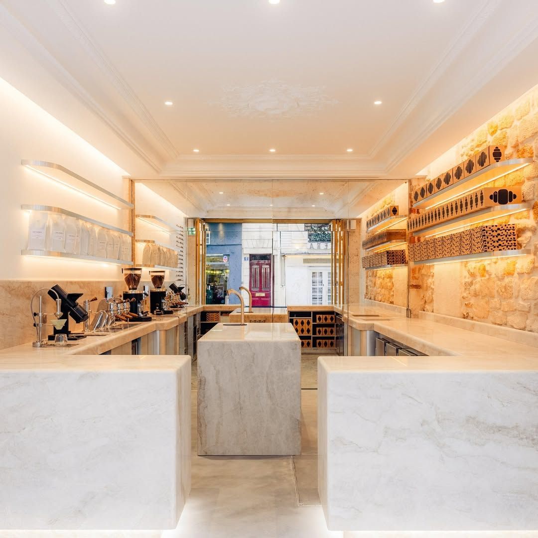 Intérieur d'un café avec comptoir en marbre, machines à café et étagères de produits ; porte ouverte.