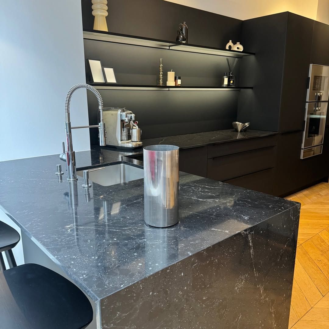 Cuisine moderne noire avec îlot central, robinet en acier inoxydable et plan de travail noir à motif moucheté.