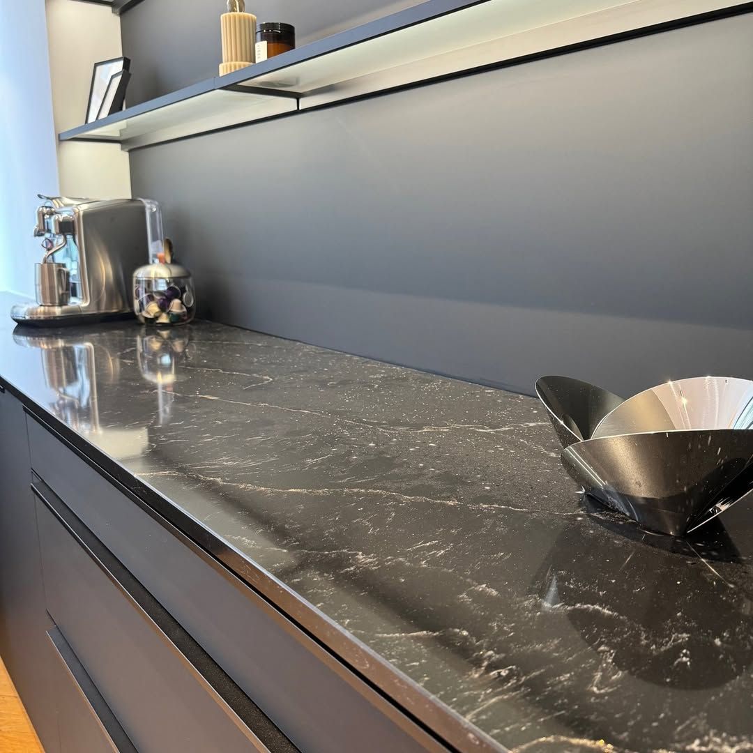 Un plan de travail foncé avec un bol métallique, des appareils électroménagers en acier inoxydable et un mur gris dans une cuisine moderne.