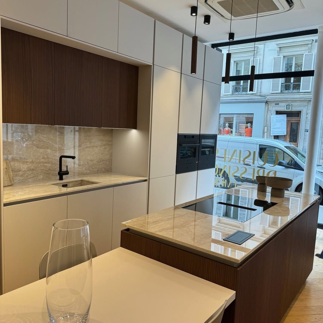 Cuisine moderne avec armoires claires, éléments en bois et îlot central. Grande fenêtre avec vue sur la ville.