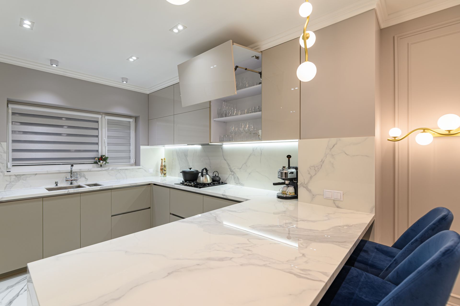 Cuisine moderne avec placards gris clair, comptoirs en marbre et tabourets de bar en velours bleu.